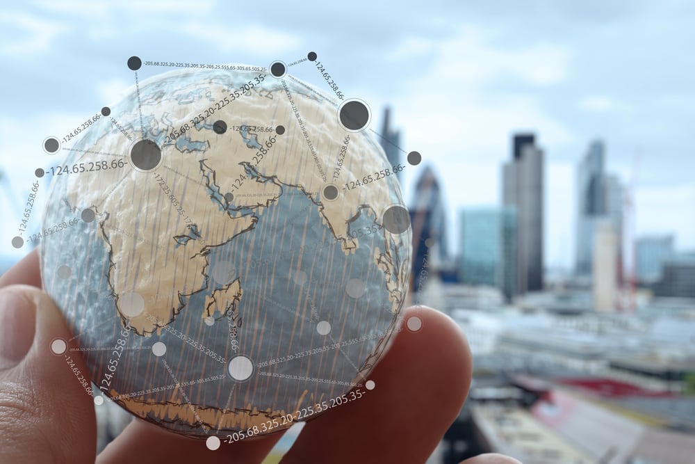 Closeup of a data privacy expert's hand holding a small globe in front of a city skyline to illustrate our global overview of data privacy compliance.